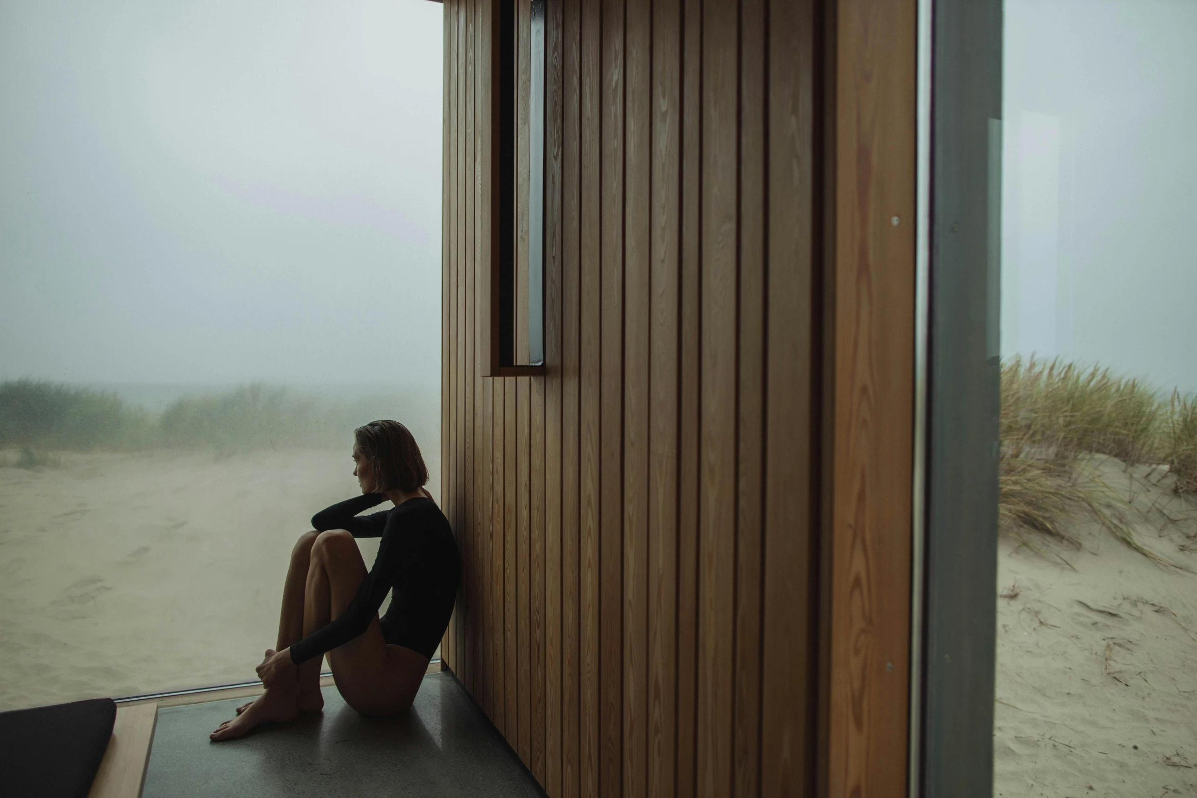 a girl sitting against a building and looking out at the beach