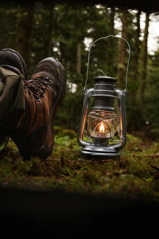 a person standing next to a lit lantern in the forest