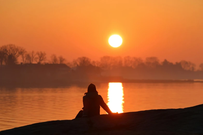 person sitting on a rock looking out at a sunset over water