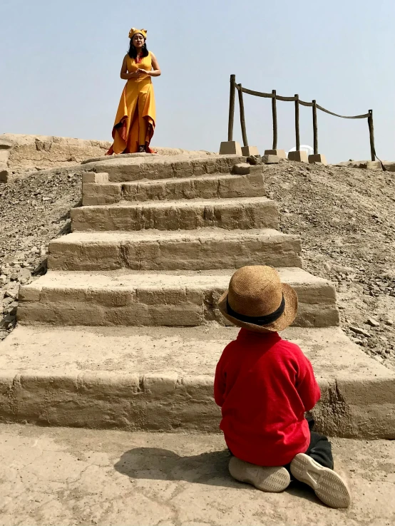 child wearing a hat sitting on a stairs in front of a statue