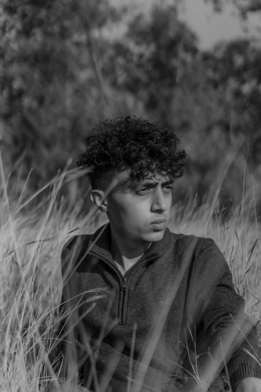 a  with curly hair sitting in tall grass