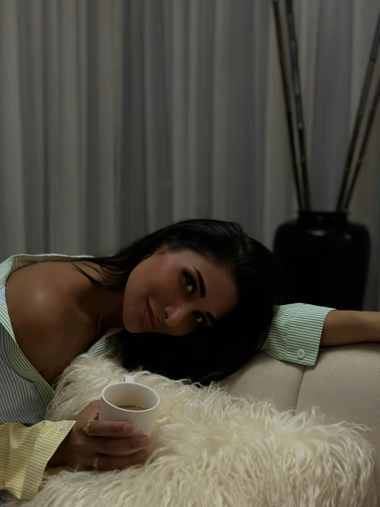 a girl holding a coffee cup while leaning on the back of a couch