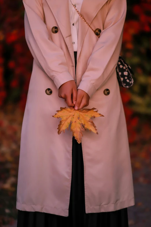 a woman in a pink coat holding a yellow autumn leaf