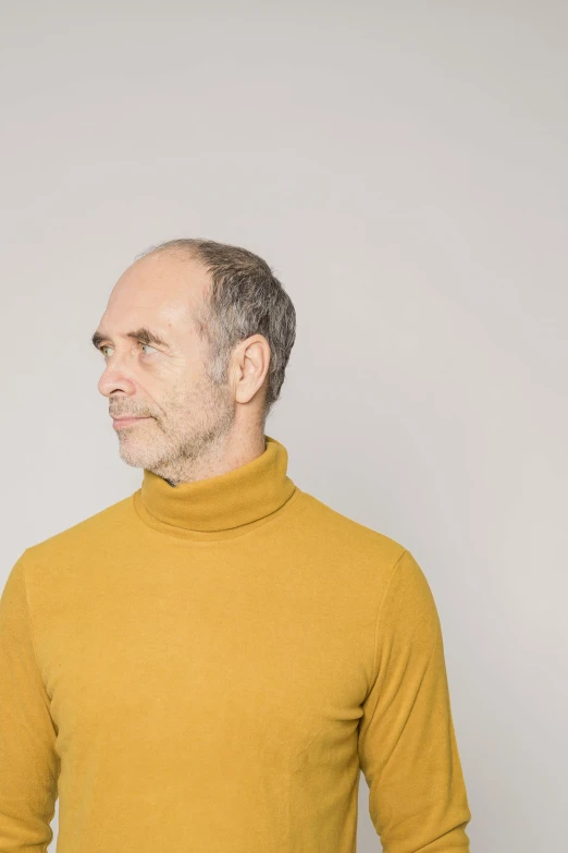 a man in yellow sweater standing with his hands behind his back