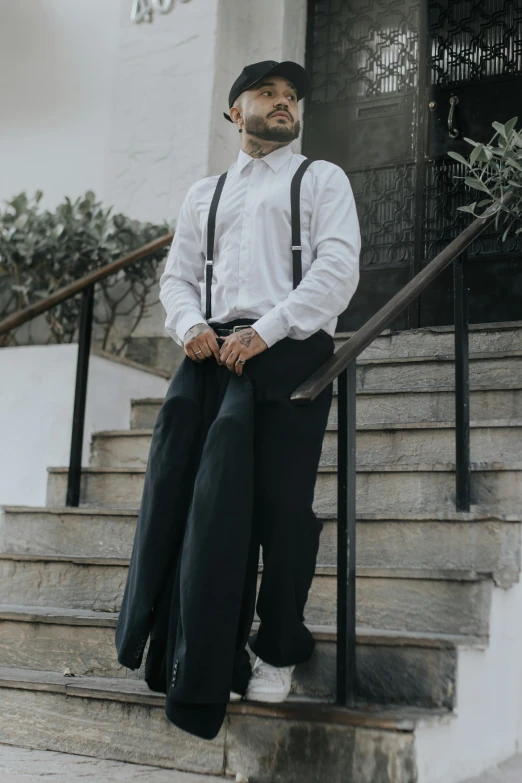 a man wearing suspenders and a hat standing in front of some stairs