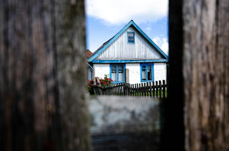 a white building with a blue roof, seen through the gap in a fence