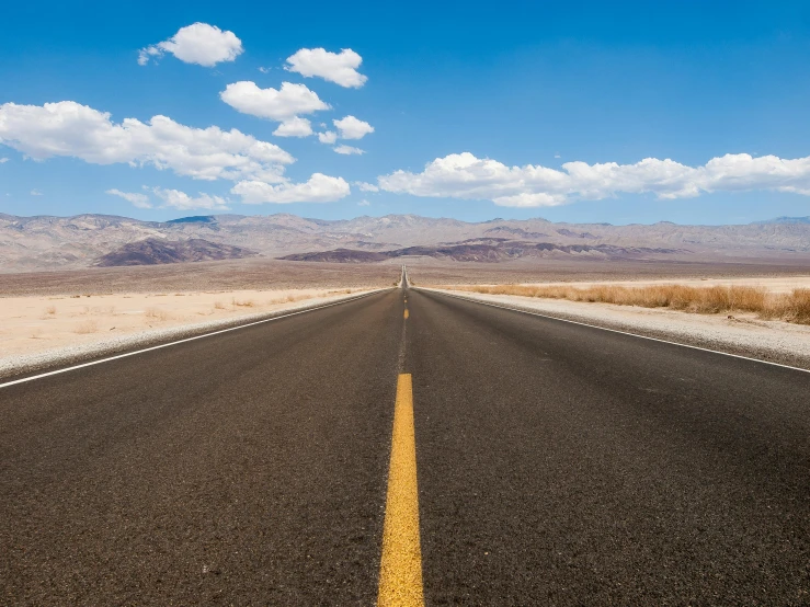 a long stretch of asphalt road with mountains in the distance