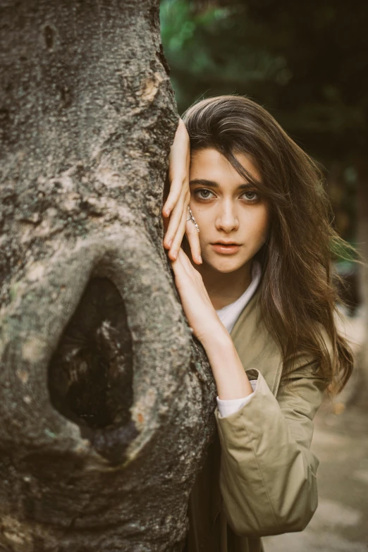 a girl leaning up against the back of a tree