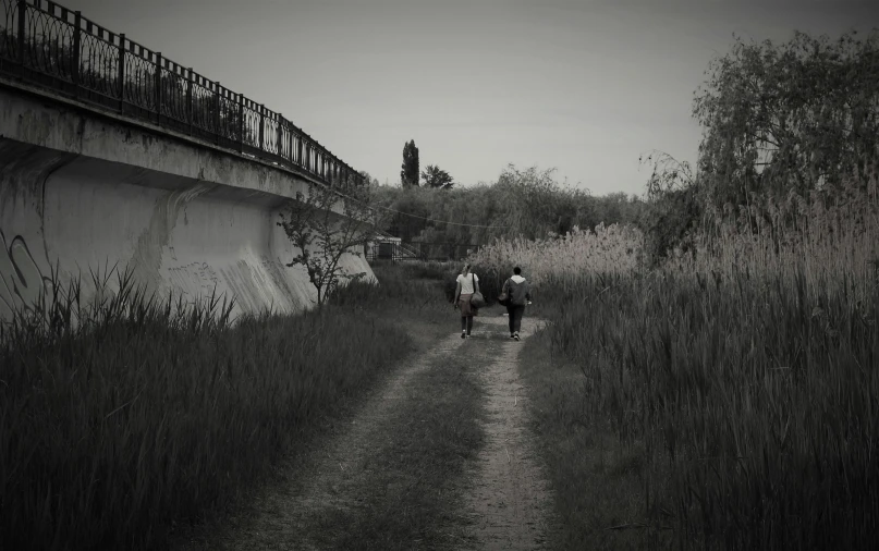 two people walking down a path on the side of a bridge