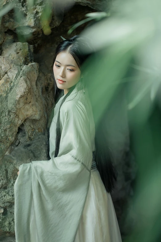 an asian girl dressed in white, leaning against a stone wall