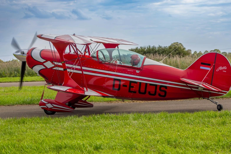 a red airplane is on the ground by some grass