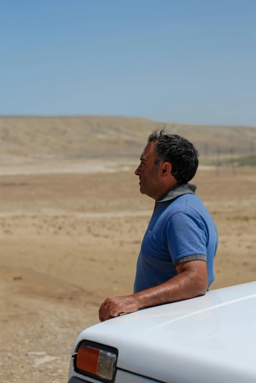 a man in blue shirt leaning on the back of a car