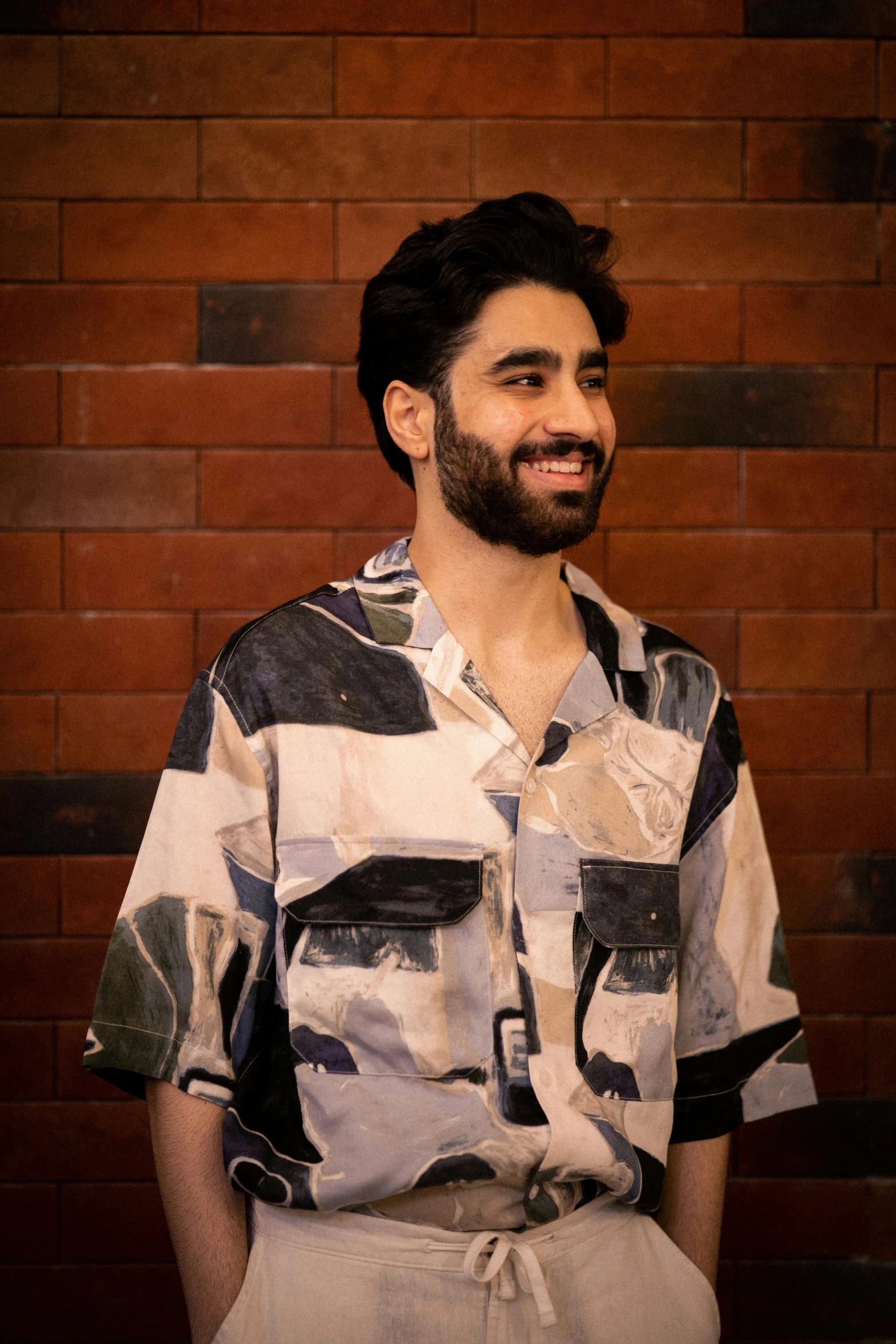 a man in a shirt smiles next to a brick wall