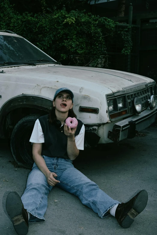 the young woman is sitting on the ground eating a donut