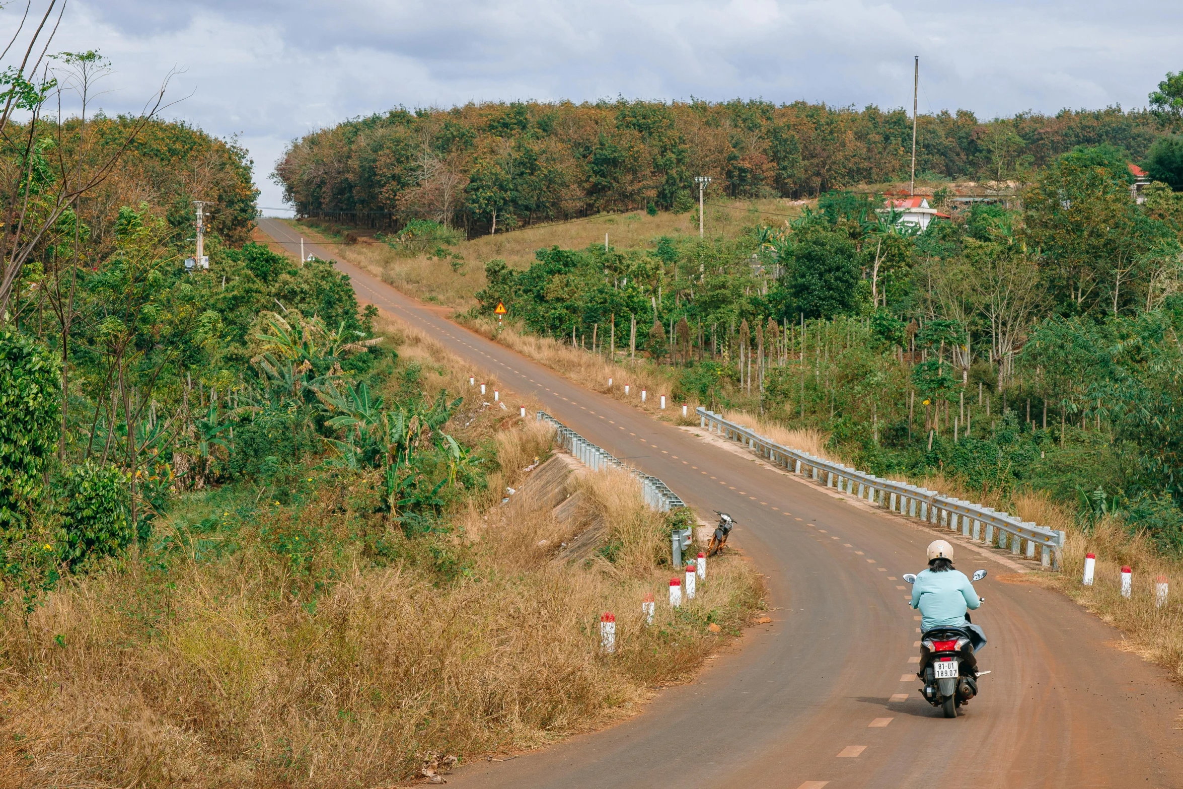 a man riding on the back of a red motorcycle down a country road