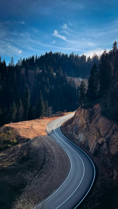 an empty road running alongside a rocky cliff