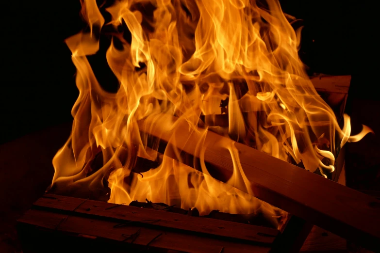 flames are spread over some wood in the dark