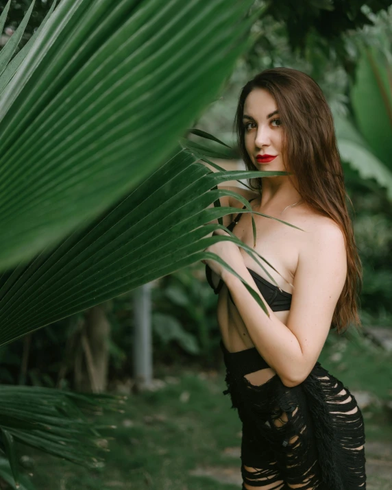 a woman in lingerie holding onto a large green palm leaf