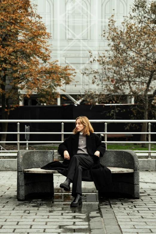 a woman sitting on top of a bench with her hands in her pockets