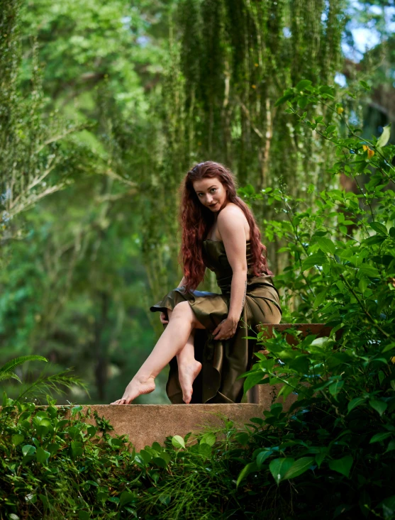 a woman with long red hair is posing on a rock