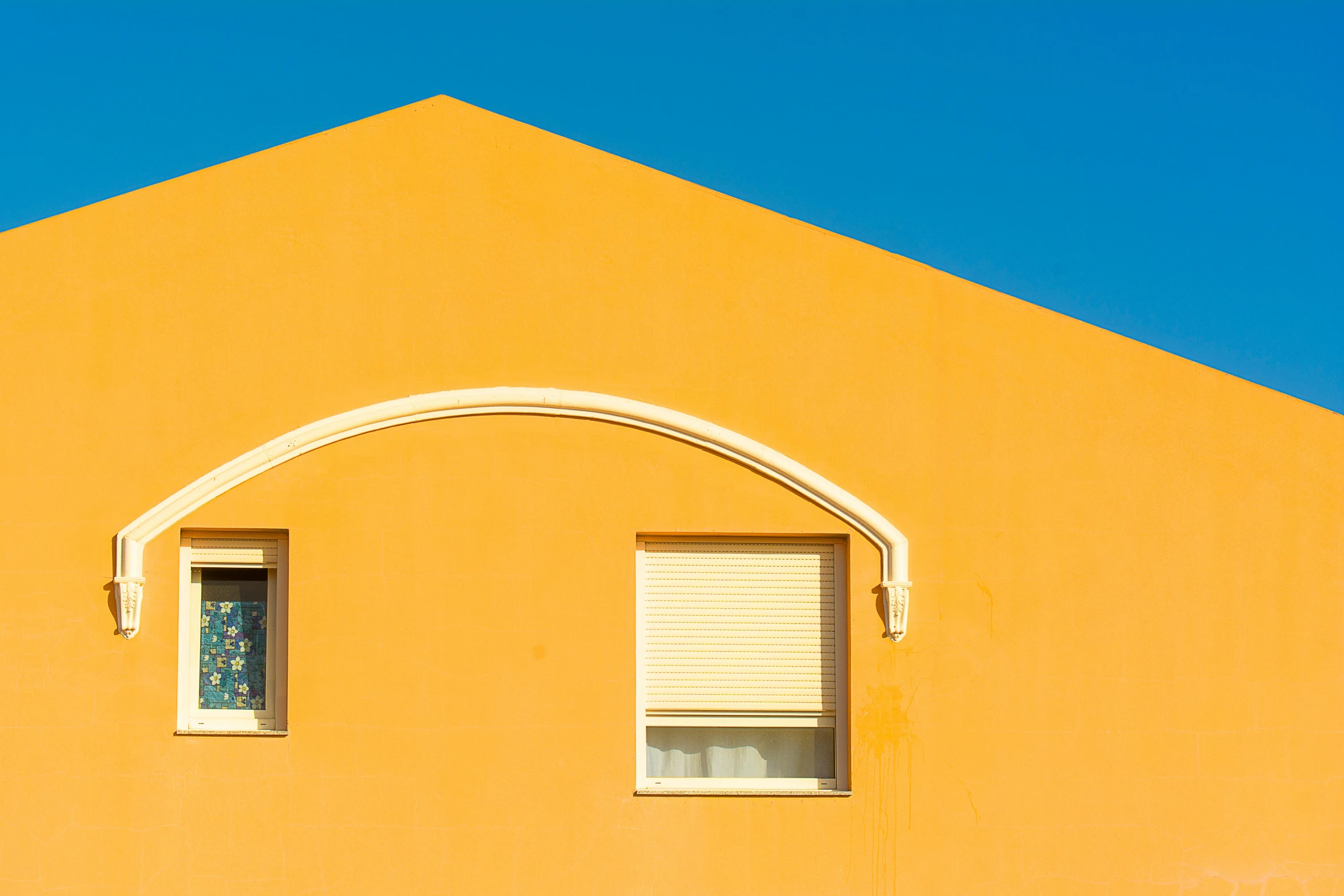 two windows of an orange building with blue sky behind them