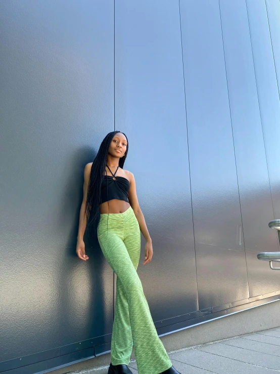 a woman standing next to a wall in cropped green pants