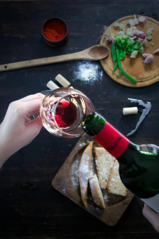 wine being poured into a glass with food on a  board and chopsticks