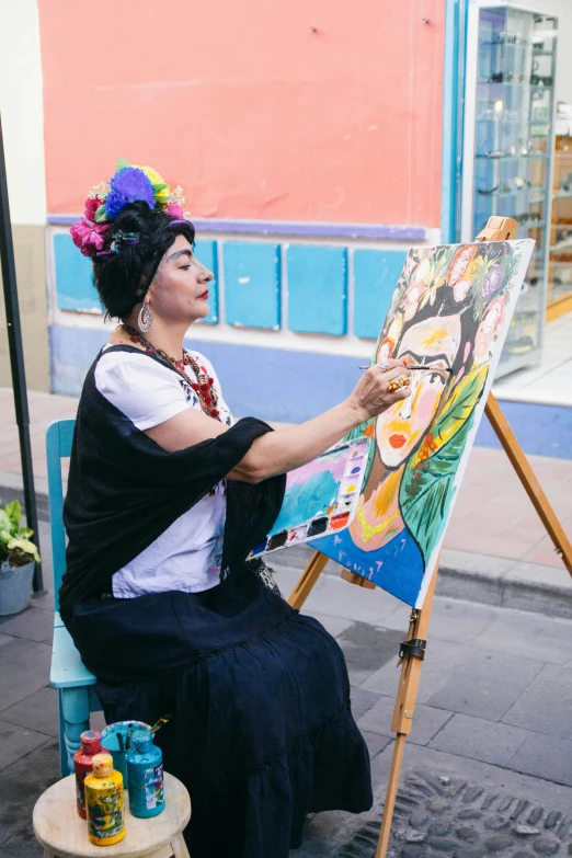 a woman in brightly colored headpiece sitting next to a large easel