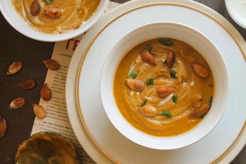 bowls of soup with nuts and greens next to one bowl on a menu