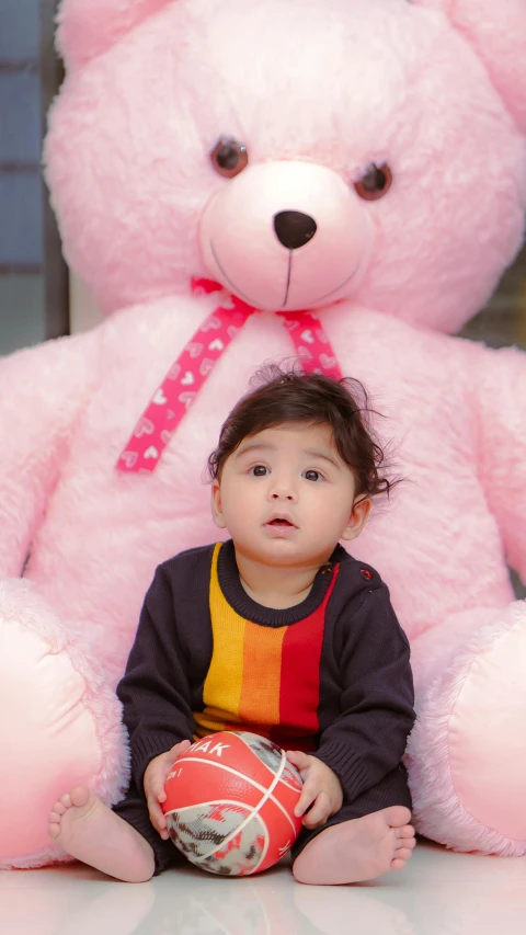 a toddler sitting in front of a giant pink teddy bear