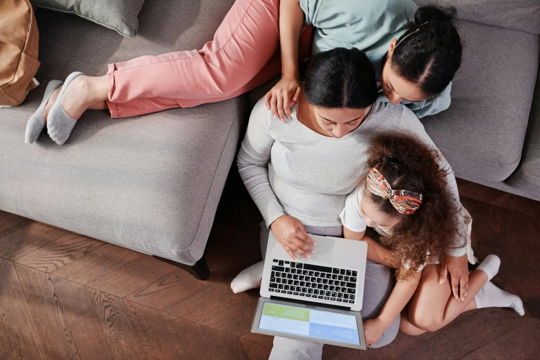 three women sitting on a couch, one using a laptop