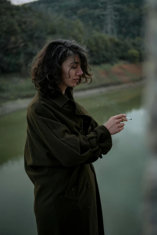 a young woman smokes a cigarette near the river