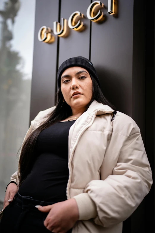 an overweight woman standing against a wall with the letters gucci above her