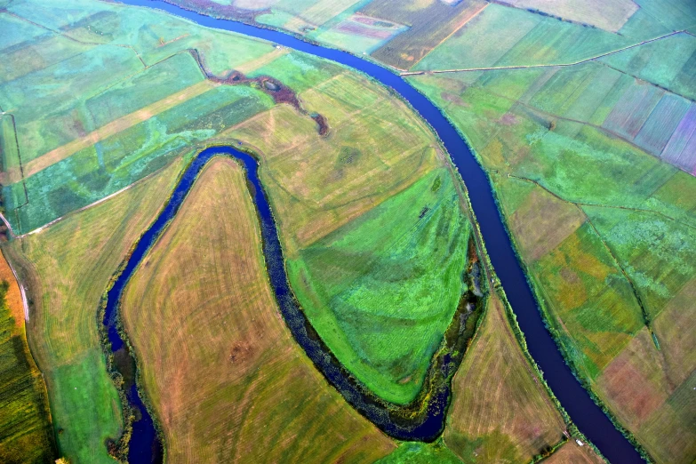 aerial po taken from the top of an airplane shows a river running through green fields and rolling into the distance