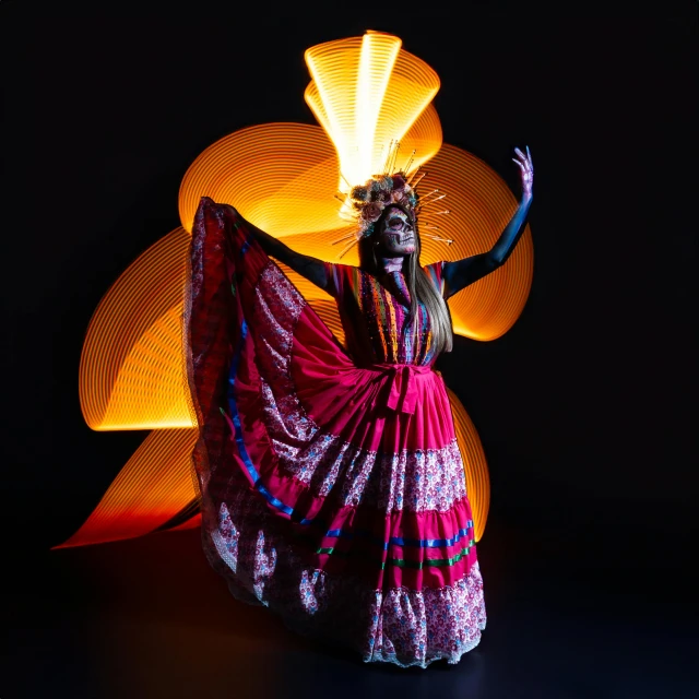 the woman wearing a colorful dress is dancing with a bright orange disc behind her