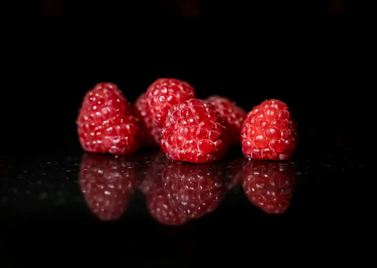 fresh raspberries are on a shiny black surface