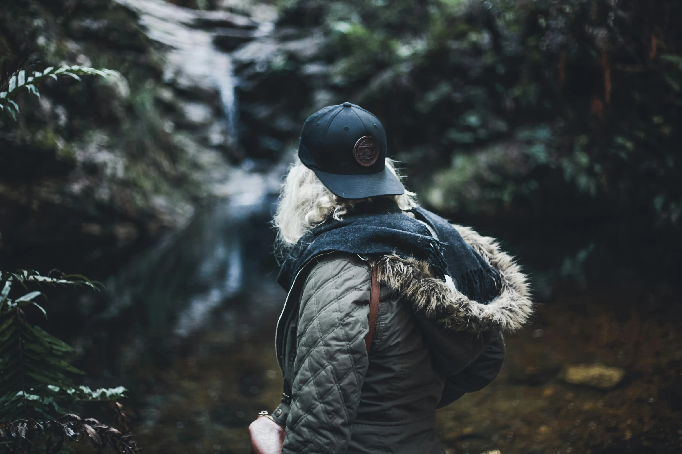 a man wearing a black jacket is standing near a waterfall