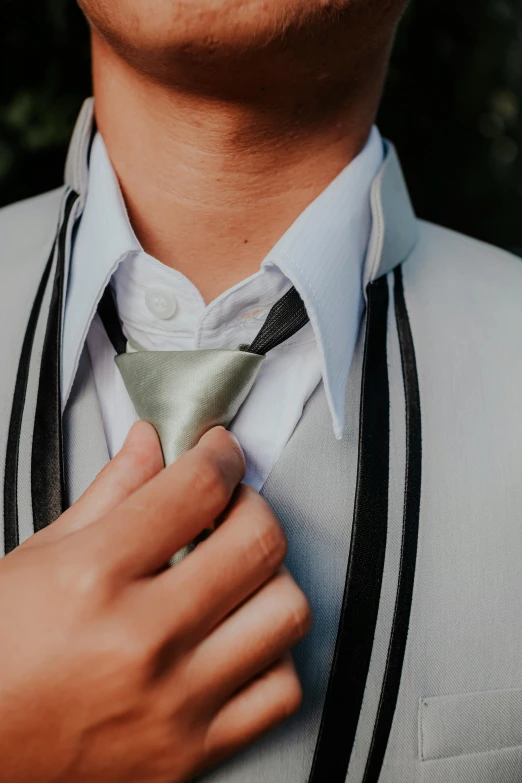 a close - up of a man adjusts a tie on his suit jacket