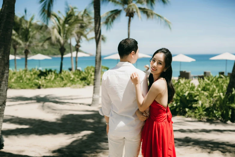 man in white suit hugging woman in red dress on the beach