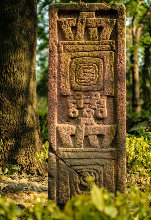 the large cement head in front of a tree is adorned with ancient symbols