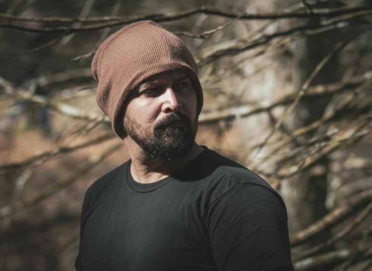 a man with beard and cap in front of tree nches