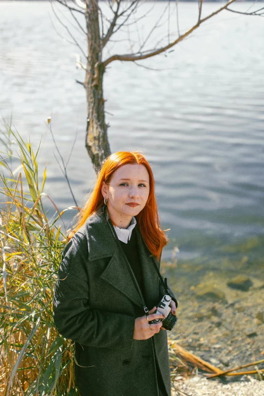 a girl with long red hair leaning on the wall near a lake