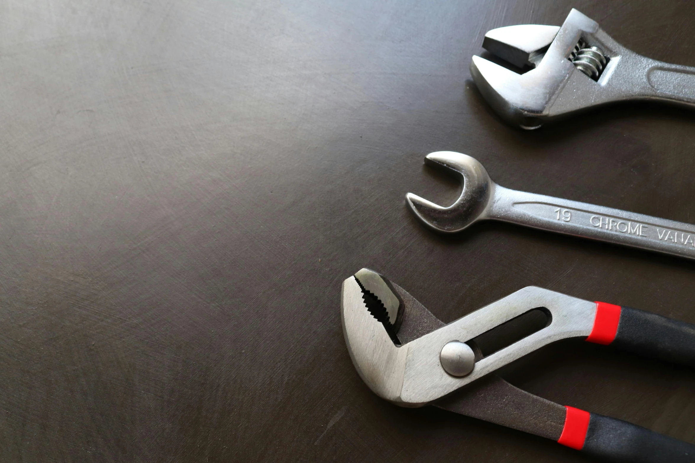 three wrenches and a pliers laying on a black table