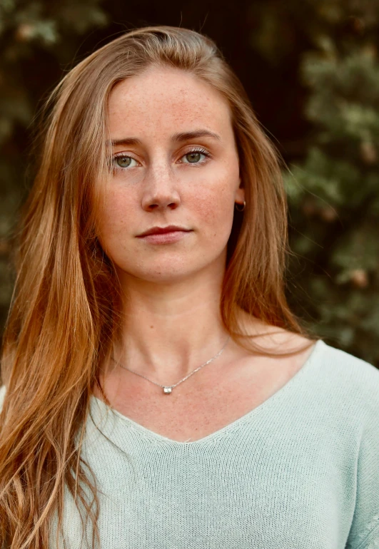 a woman looking into the camera in front of trees