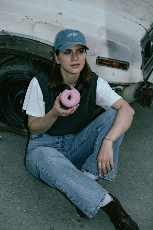 a woman eating a pink donut next to a white car