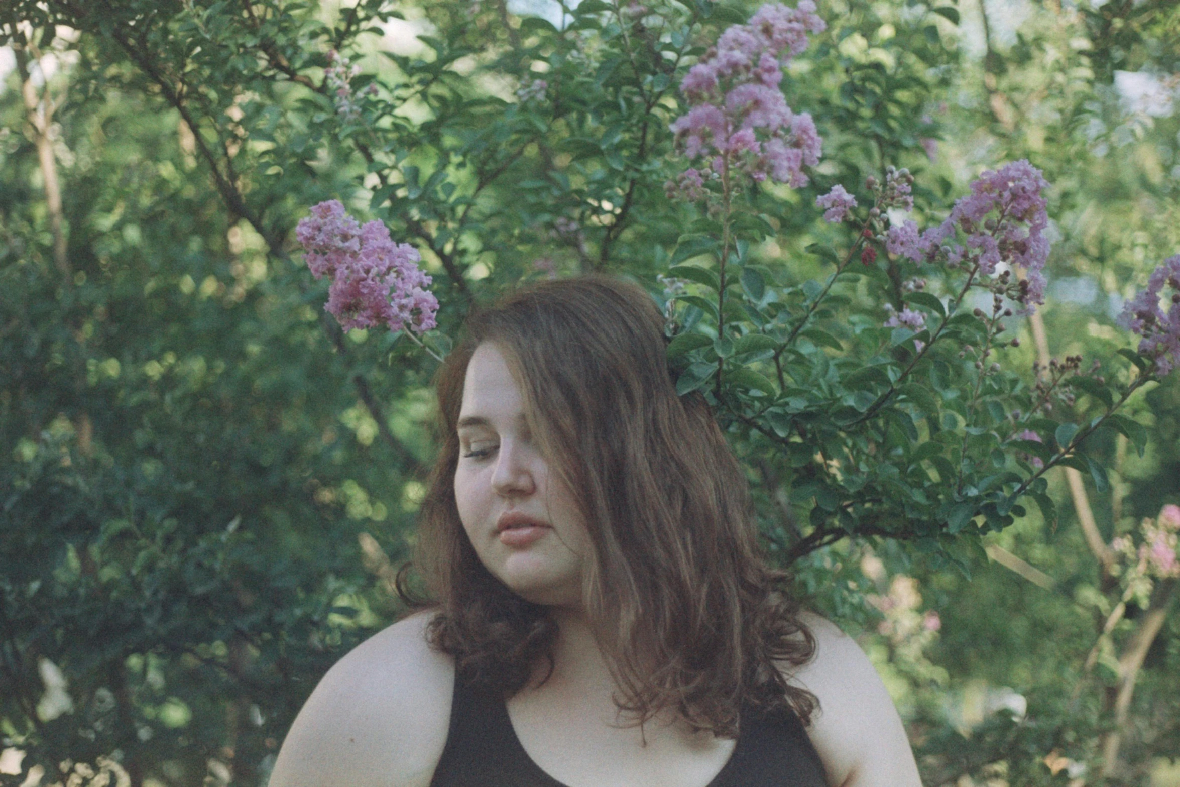 a woman in black top standing by a bush with flowers