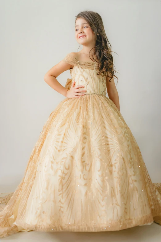 a little girl in a gold gown standing in front of a white background