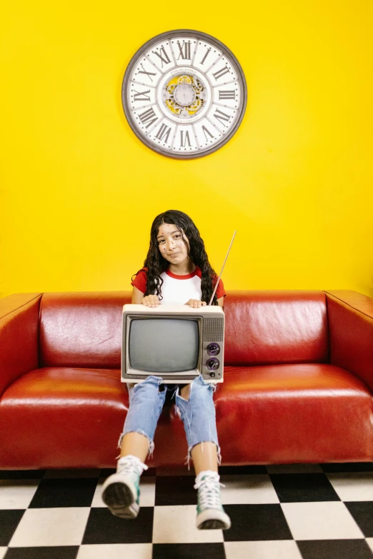 the girl is sitting on a red couch with a television