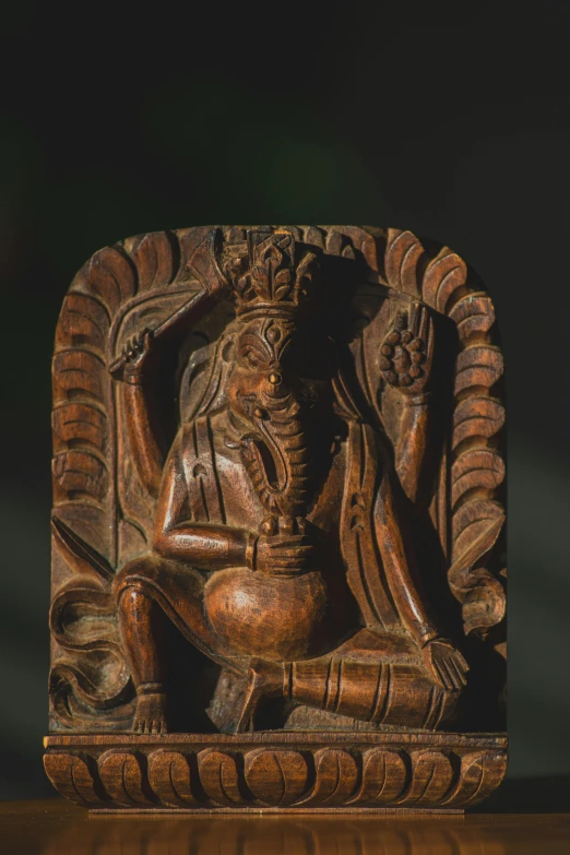 a carving in wood depicting a female figure sitting on a stool