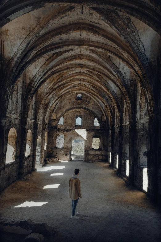 a man in a white jacket walks down a stone hallway in a ruined castle